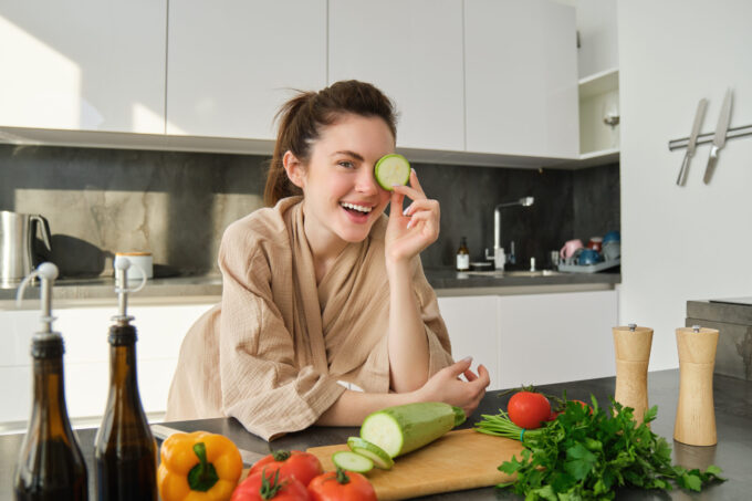 Portrait of brunette woman, wife cooking at home, making dinner, posing near chopping board in kitchen with vegetables, holding zucchini