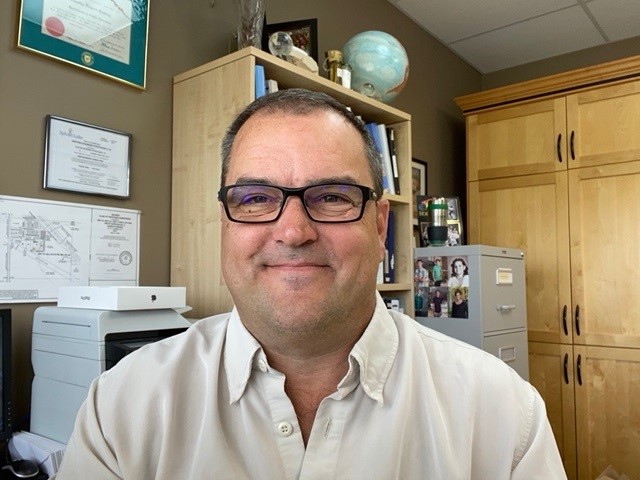Tim Keating, a white man with short dark hair, smiles at the camera in an office. He is wearing a light-coloured dress shirt and glasses with dark frames.
